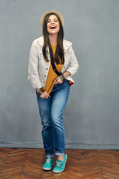 Smiling woman casual dressed standing in front of grey wall. Full body portrait.