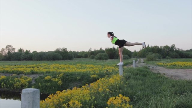 A purposeful woman stands on one leg and performs yoga exercises. The girl is engaged in sports at sunset. Steadicam shot