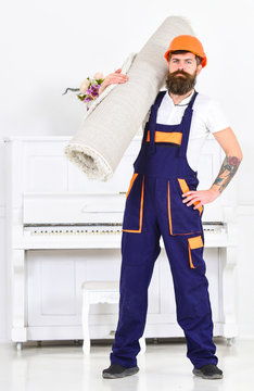 Full length portrait of man isolated in white painted room. Builder with tattoo on arm holding rolled carpet on his shoulder