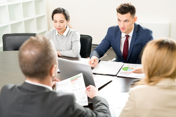 Fototapeta premium High angle view at business meeting with handsome young man explaining partnership terms to colleagues sitting at table in conference room