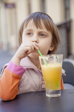 Little beautiful girl child drinks orange. (Vitamins, health, thirst, happy childhood concept)