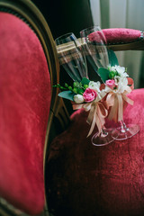 Wedding glasses decorated with cord and flowers, beautiful green ribbon on wedding glasses, handmade wedding glasses on red vintage chair.