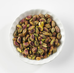 PISTACHIO NUT KERNELS IN WHITE BOWL ON WHITE BACKGROUND