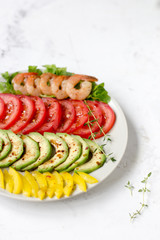 Avocado salad on a white background. Avocado, tomato, pepper and shrimps on a plate lined with rows