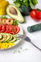 Avocado salad on a white background. Avocado, tomato, pepper and shrimps on a plate lined with rows