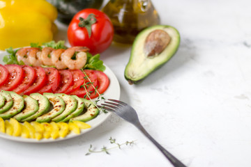 Avocado salad on a white background. Avocado, tomato, pepper and shrimps on a plate lined with rows
