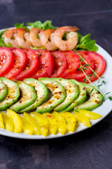 Avocado, tomato, pepper and shrimps on a plate lined with rows. Avocado salad on a dark background