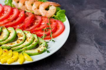Avocado, tomato, pepper and shrimps on a plate lined with rows. Avocado salad on a dark background