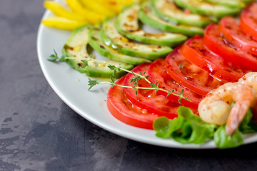 Avocado, tomato, pepper and shrimps on a plate lined with rows. Avocado salad on a dark background