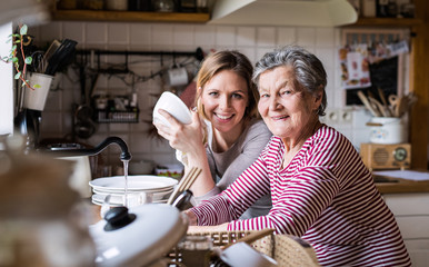 An elderly grandmother with an adult granddaughter at home, washing the dishes.