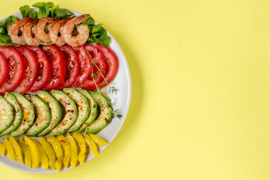 Avocado salad on a yellow background. Avocado, tomato, yellow paprika and shrimps on a plate
