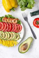 Avocado salad on a white background. Avocado, tomato, pepper and shrimps on a plate lined with rows