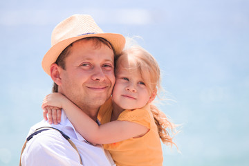 Happy little girl hugging father. Cheerful young man with child close-up on sea background.