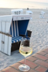 Glas of white wine in front of a traditional roofed wicker beach chair on the island of Sylt
