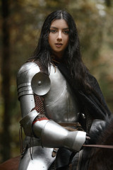 A beautiful warrior girl with a sword wearing chainmail and armor riding a horse in a mysterious...
