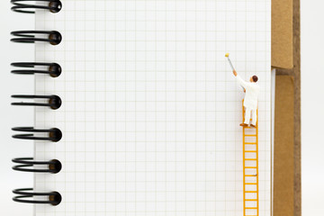 miniature people: mini figure with ladder and white paint in front of a book.