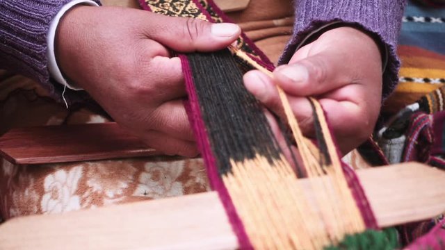 Indigenous woman selects the yarn meanwhile weaves yarn a foot loom at downtown Cusco, Peru.