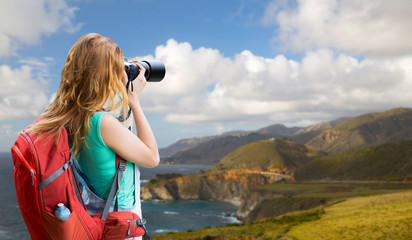 travel, tourism and photography concept - happy young woman with backpack and camera photographing over bixby creek bridge on big sur coast of california background