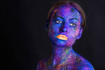 Creative make-up and beauty theme: beautiful girl model with cosmic make-up on face and body blue and purple skin color on dark background in studio