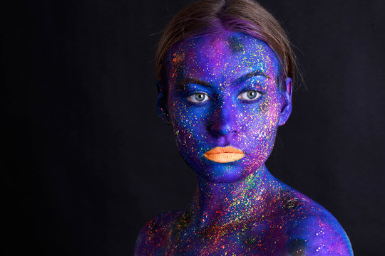 Creative make-up and beauty theme: beautiful girl model with cosmic make-up on face and body blue and purple skin color on dark background in studio