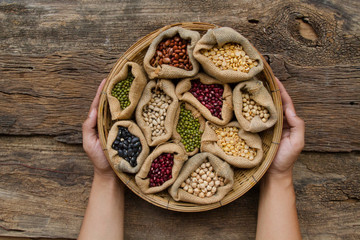legumes in wooden basket holding by hand on wooden background, top view