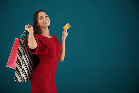 Happy young woman with credit card and shopping bags on color background