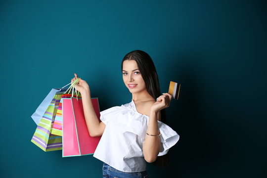 Happy young woman with credit card and shopping bags on color background