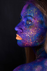 Young artistic woman in black paint and colourful powder. Glowing dark makeup. Creative body art on the theme of space and stars. Bodypainting project: art, beauty, fashion.