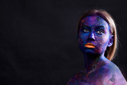Young artistic woman in black paint and colourful powder. Glowing dark makeup. Creative body art on the theme of space and stars. Bodypainting project: art, beauty, fashion.
