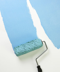 PAINT ROLLER APPLYING BLUE PAINT TO WHITE SURFACE