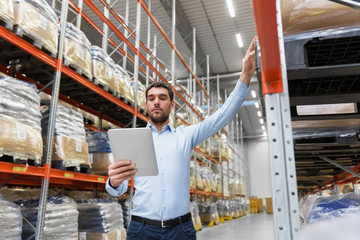 logistic business, technology and shipment concept - businessman with tablet pc computer checking goods at warehouse