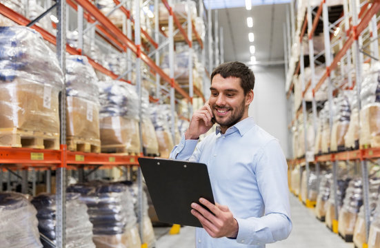 wholesale, logistic business, technology and people concept - smiling businessman calling on smartphone at warehouse