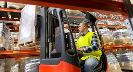 wholesale, logistic, shipment and people concept - loader operating forklift and loading boxes at...