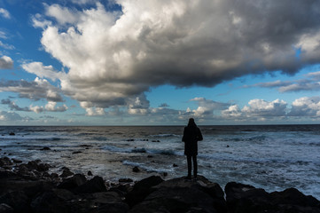 Rolling cloudscape over a silhouette of a standing man in front of sea waves