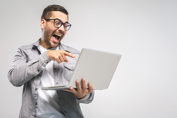 Funny young handsome man in shirt holding laptop and smiling while standing against white background. Have fun.