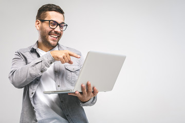Funny young handsome man in shirt holding laptop and smiling while standing against white background. Have fun.