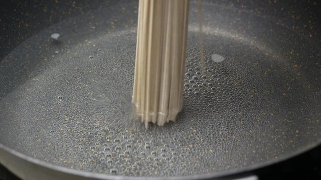 put Zaru Soba (Cold Soba Japanese Noodles food style) into boiled hot water air bubble and smokein black teflon induction pan and stir with wooden turner