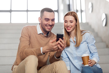 business, technology and corporate concept - smiling man and woman with smartphone drinking coffee at office stairs