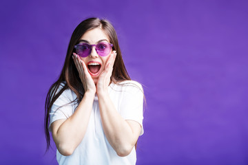 Pretty caucasian brunette girl wears sunglasses have happy surprised face expression on purple background