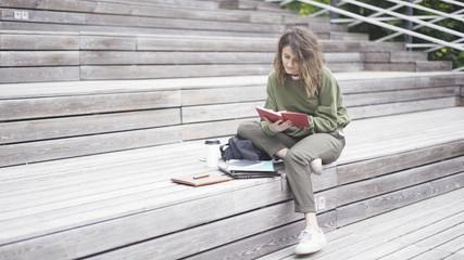 A young brunette girl dressed in a green sweat shirt is sitting on the stairs reading a book