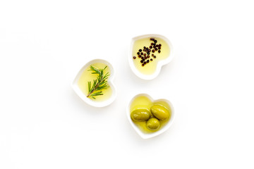 Olive oil as famous product of mediterranean cuisine. Heart shaped bowls with olive oil with green olives, rosemary and black pepper inside on white background top view copy space