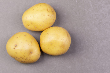 Three fresh potatoes on a gray background. Top view.
