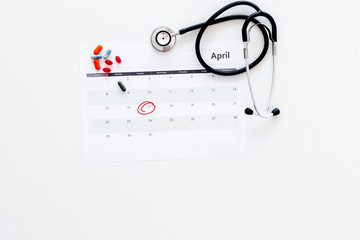 Planning medical examination concept. Regular medical examinations. Calendar with date circled, pills and stethoscope on white background top view copy space