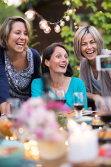Summertime. Group of friends gathered around a table in the garden to share a meal. Three beautiful women in their forties taking a selfie
