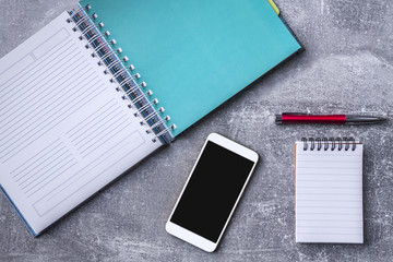A concrete desk with a notebook, a smartphone and red elegant pen