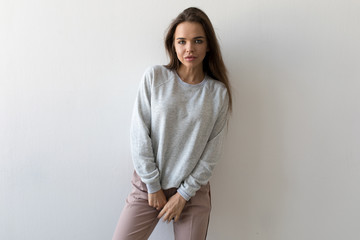 Beautiful woman in gray sweatshirt stands on white background. Mock-up.