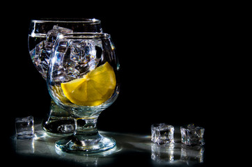 two glasses of water and lemon on a black background
