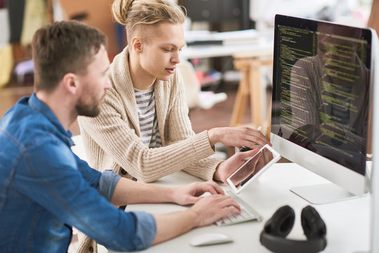 Portrait of creative young man writing code sitting at desk and  using computer while collaborating with colleague on startup project in modern office