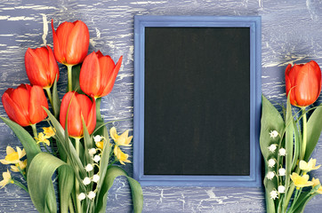 Blackboard and bunch of red tulips and lily of the valley flowers on rustic background