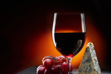 Glass of wine with grapes and a piece of cheese with mold.  Orange background.